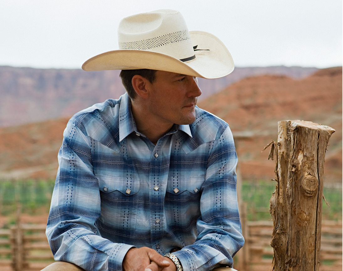 Western man leaning on fence post